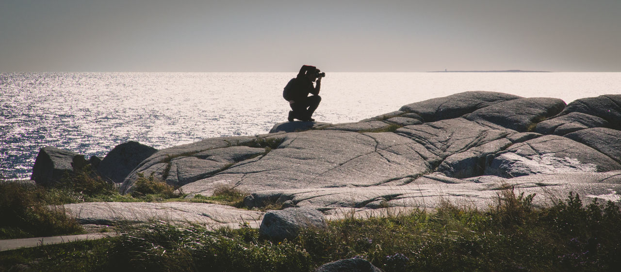 Man photographing on rock against sea