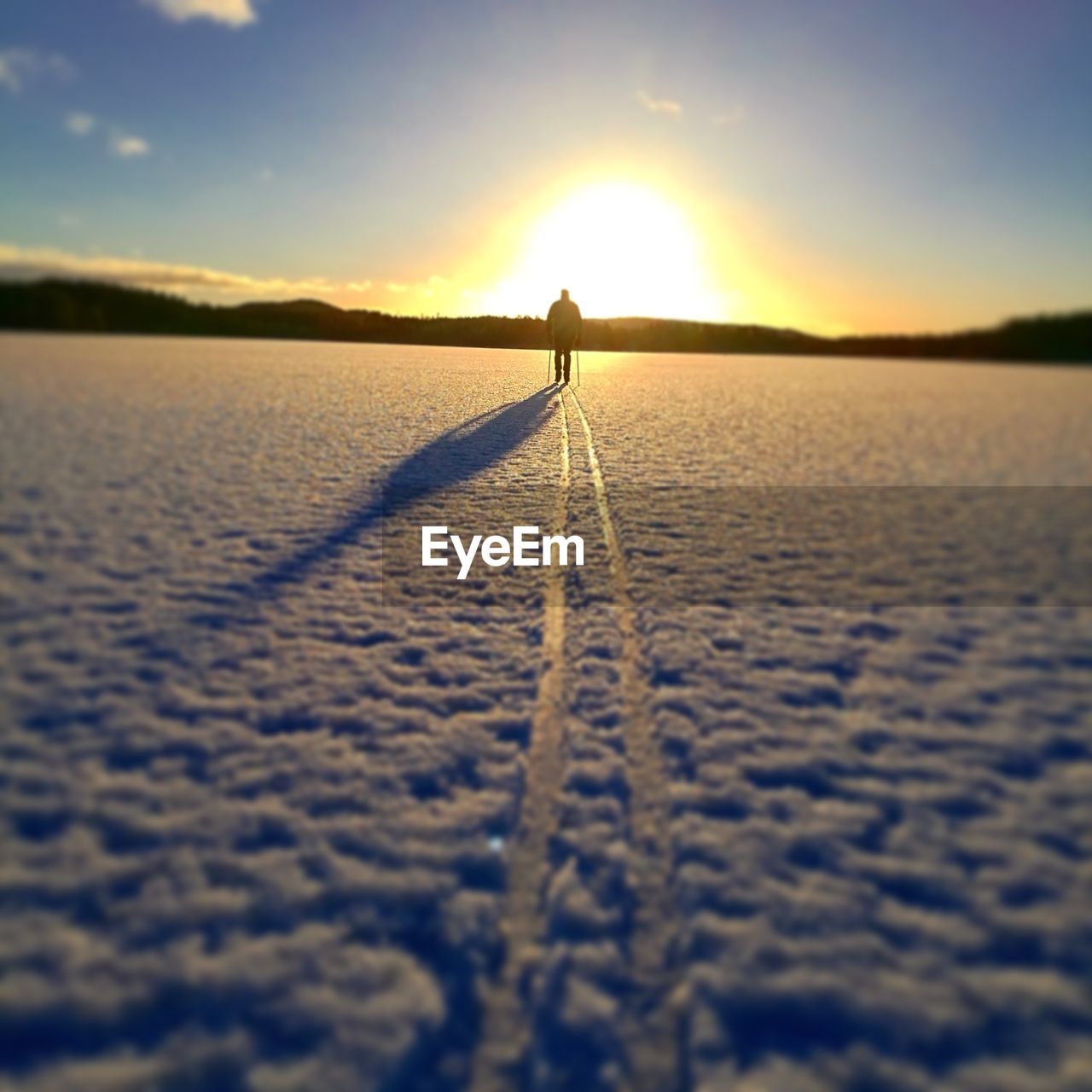 REAR VIEW OF MAN ON SNOW COVERED LANDSCAPE AT SUNSET