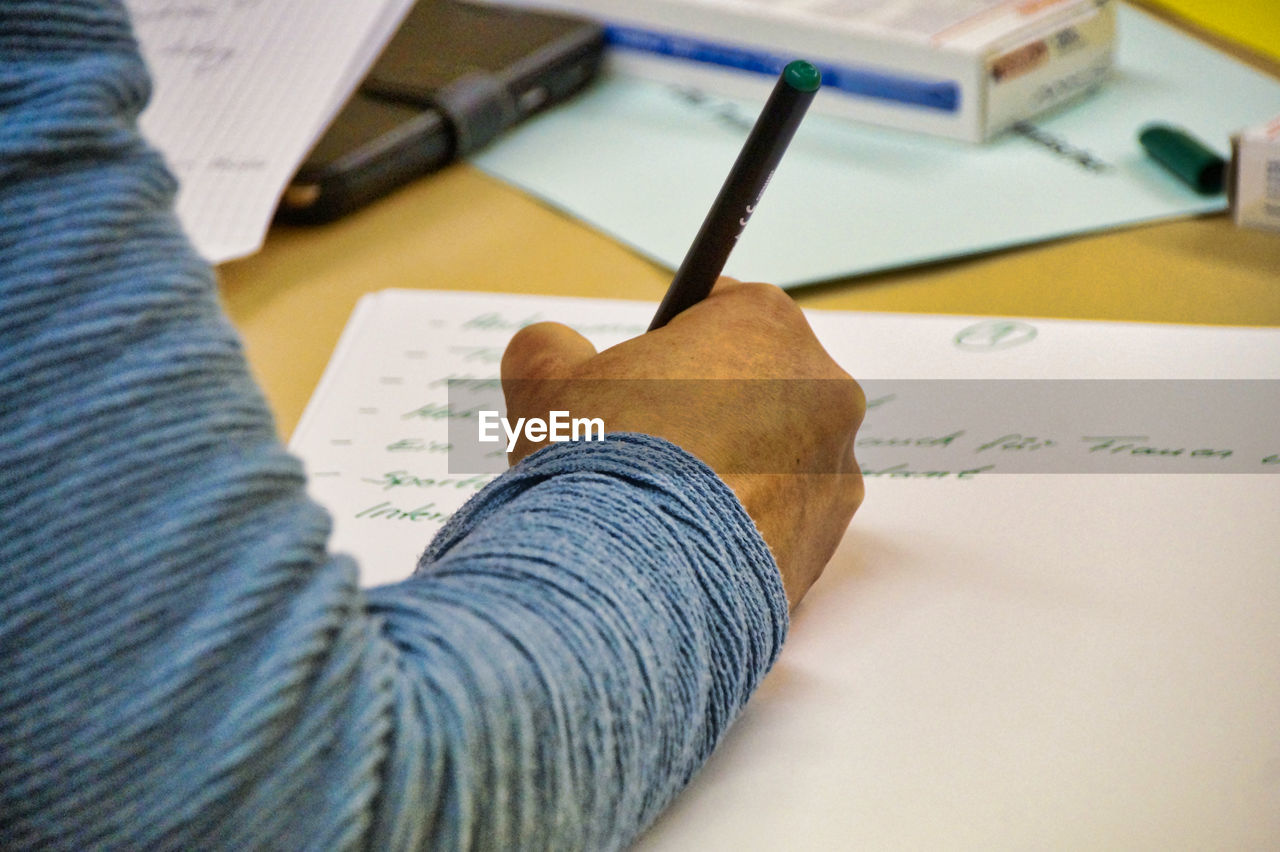 Cropped hand of man writing in paper on table