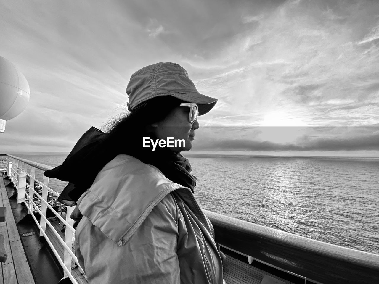 Woman wearing sunglasses while standing by railing of boat in sea against sky