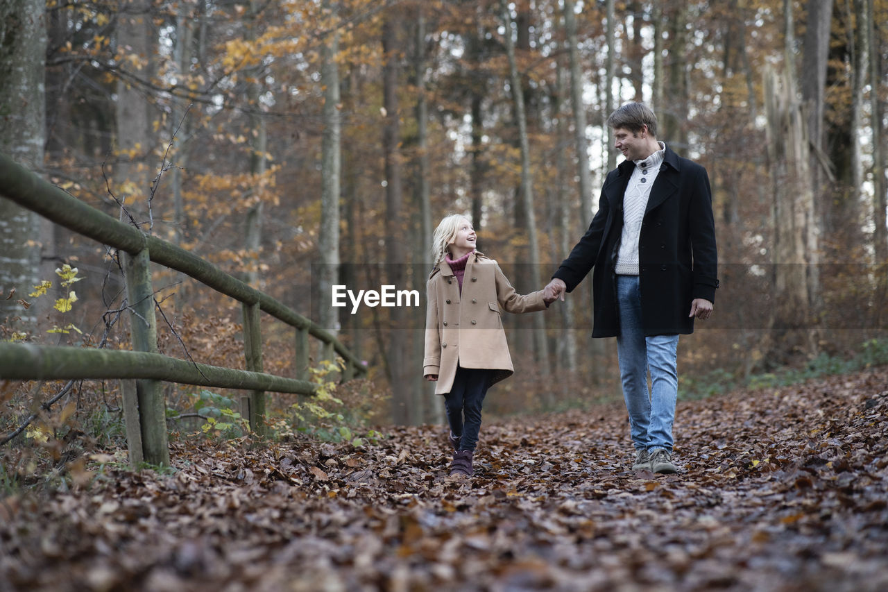 Happy girl holding hand of father and walking in autumn forest