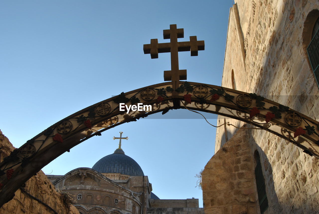 Low angle view of cross on arch entrance against sky