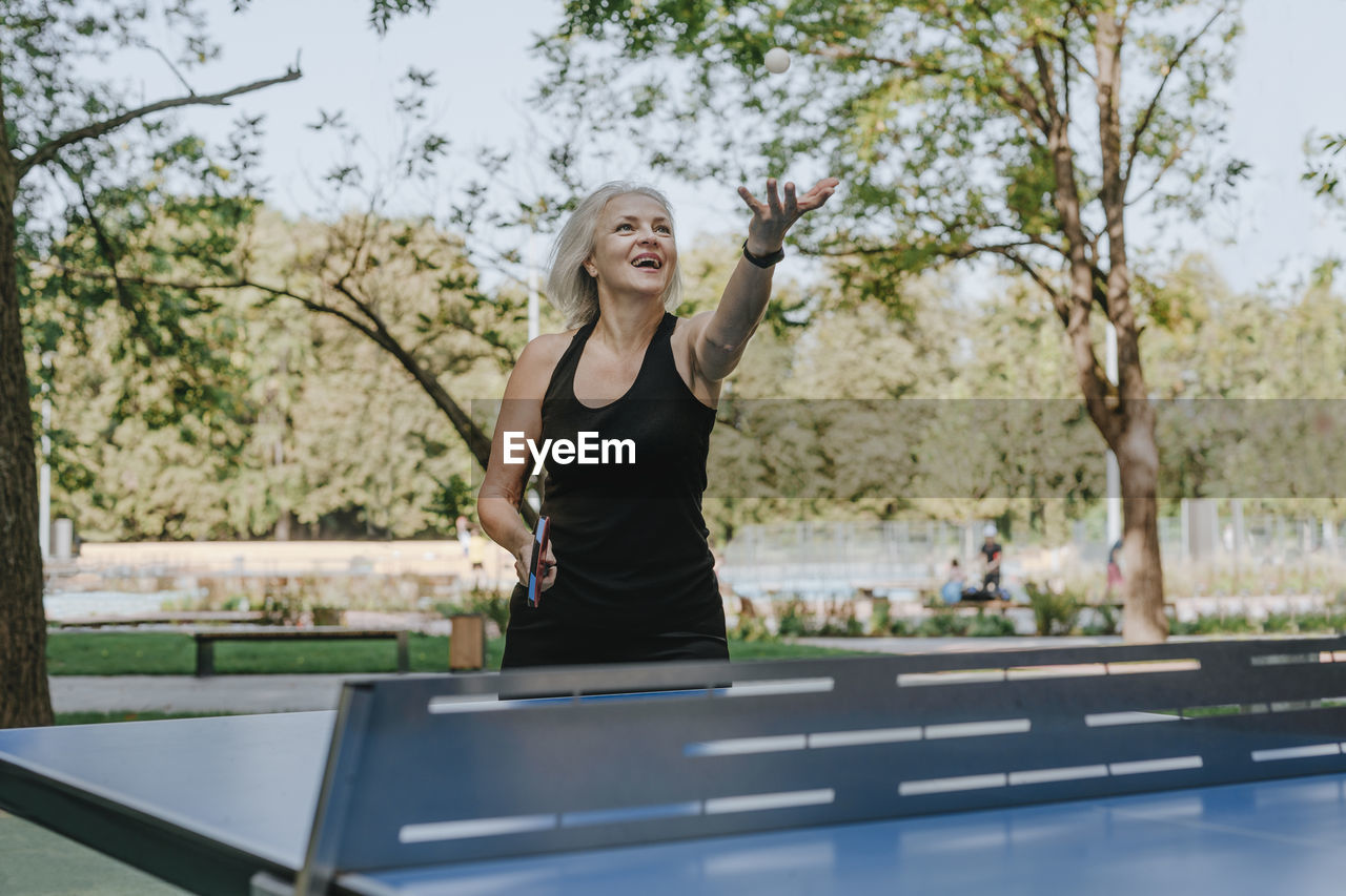 Mature woman tossing ball playing table tennis park