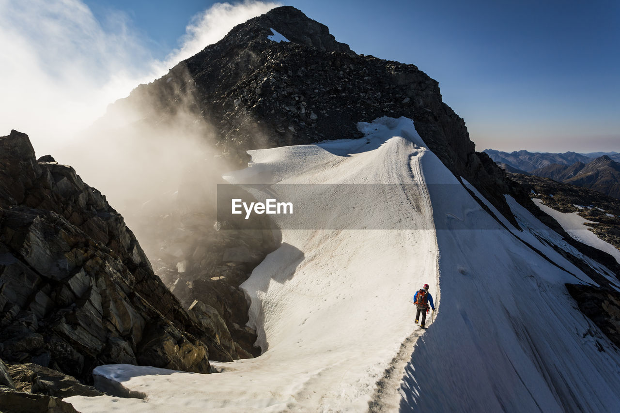 Climber traversing a snow ridge whilst mountaineering in new zealand