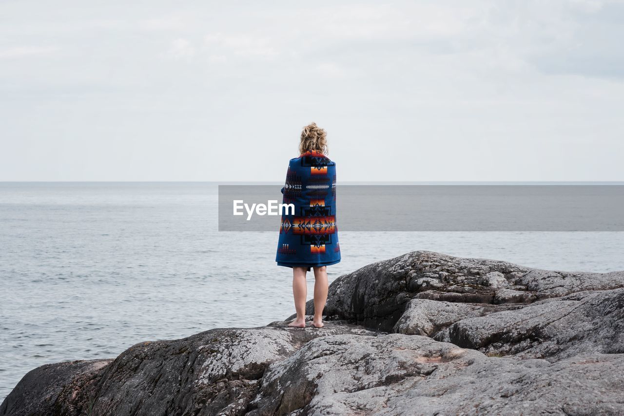 Woman standing on rocks wrapped in a pendleton blanket in sweden