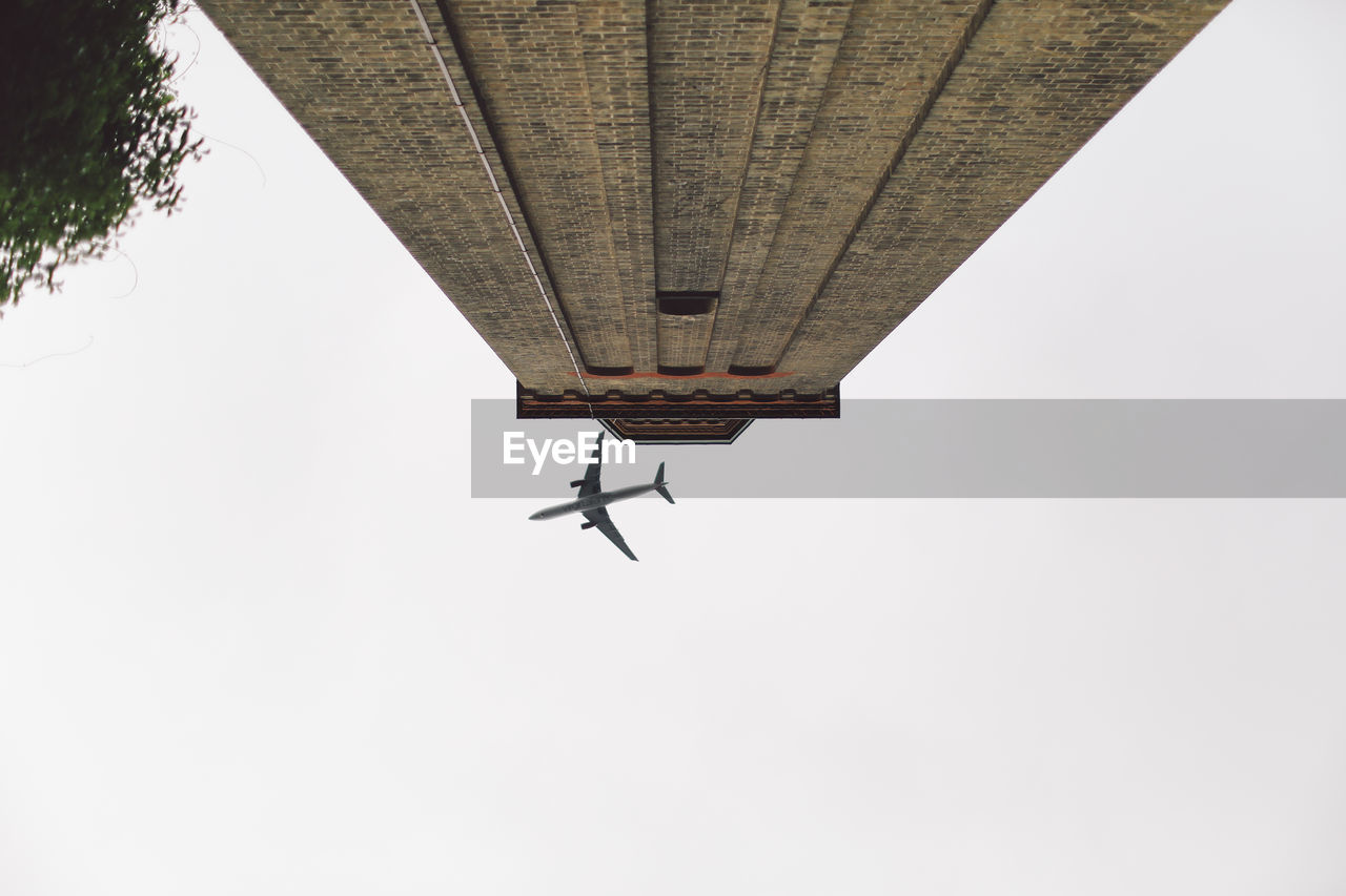 Directly below shot of airplane over building against clear sky