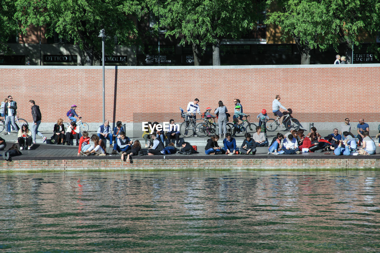 People relaxing at riverbank against wall