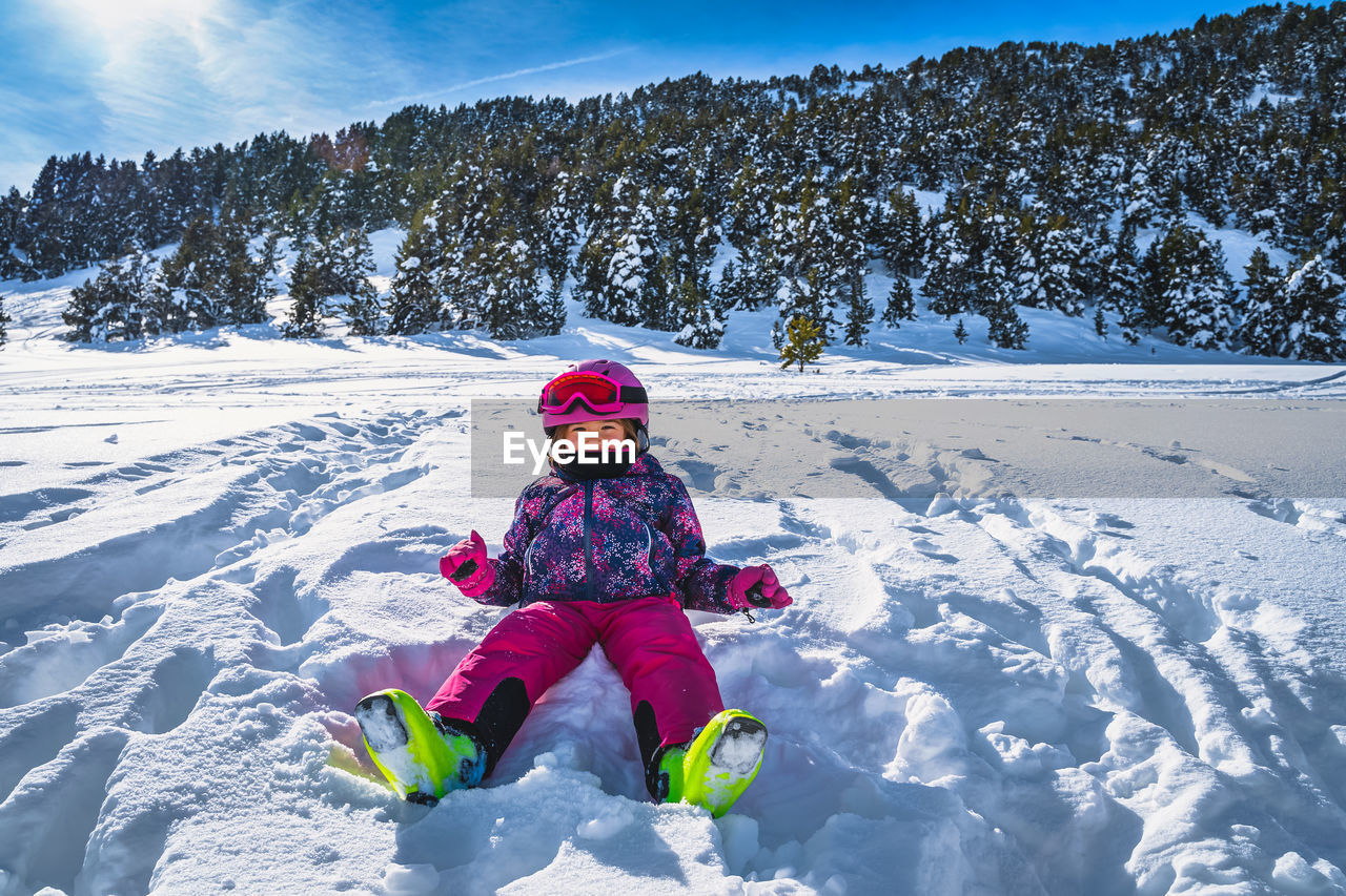 Smiling girl sitting on fresh snow with mountains and forest in a background, andorra