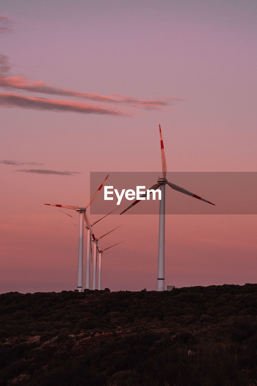 WINDMILLS ON FIELD AGAINST SKY AT SUNSET
