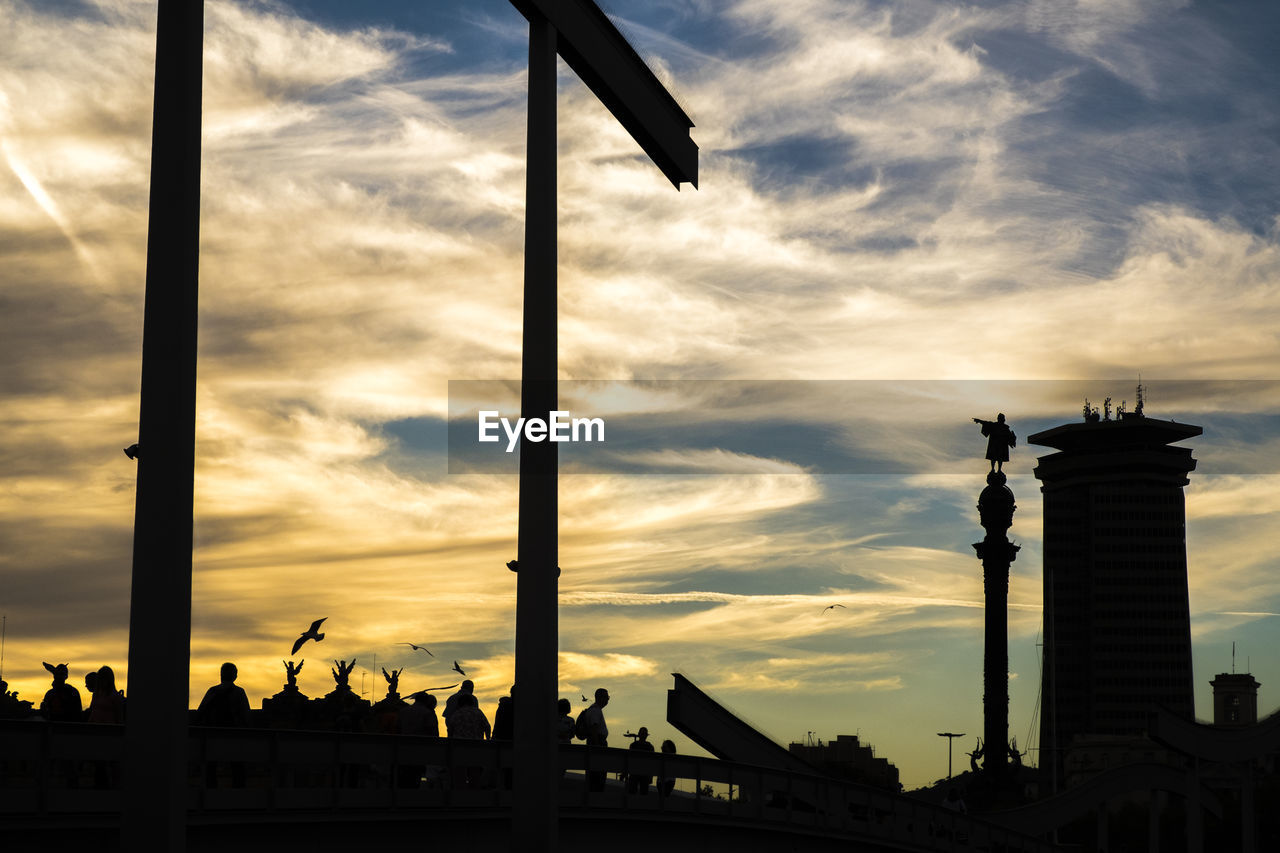 Silhouette rambla del mar bridge at port vell against cloudy sky