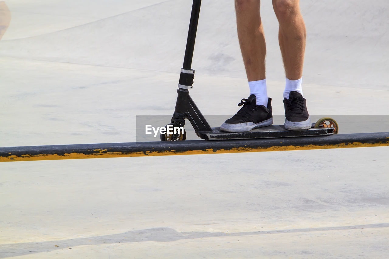 Low section of man with push scooter standing on railing