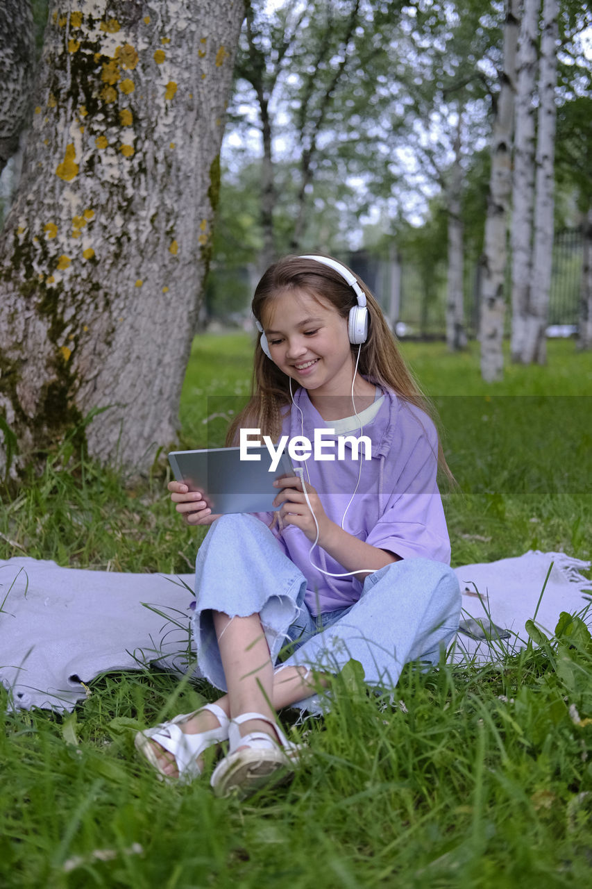 A teenage girl sits on the lawn in the park and holds a planchette in her hands