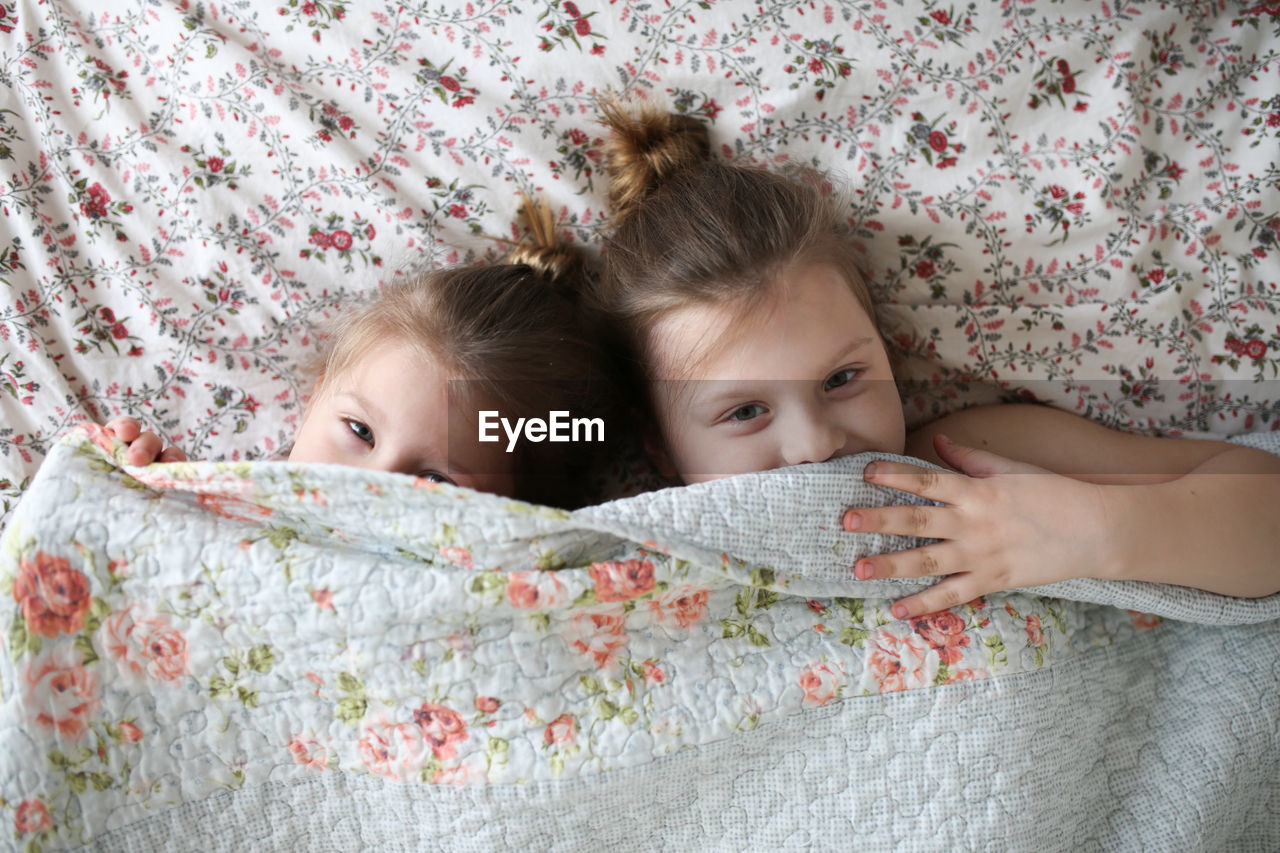 Funny children embrace, play under a blanket on the bed. concept happy childhood and siblings. 