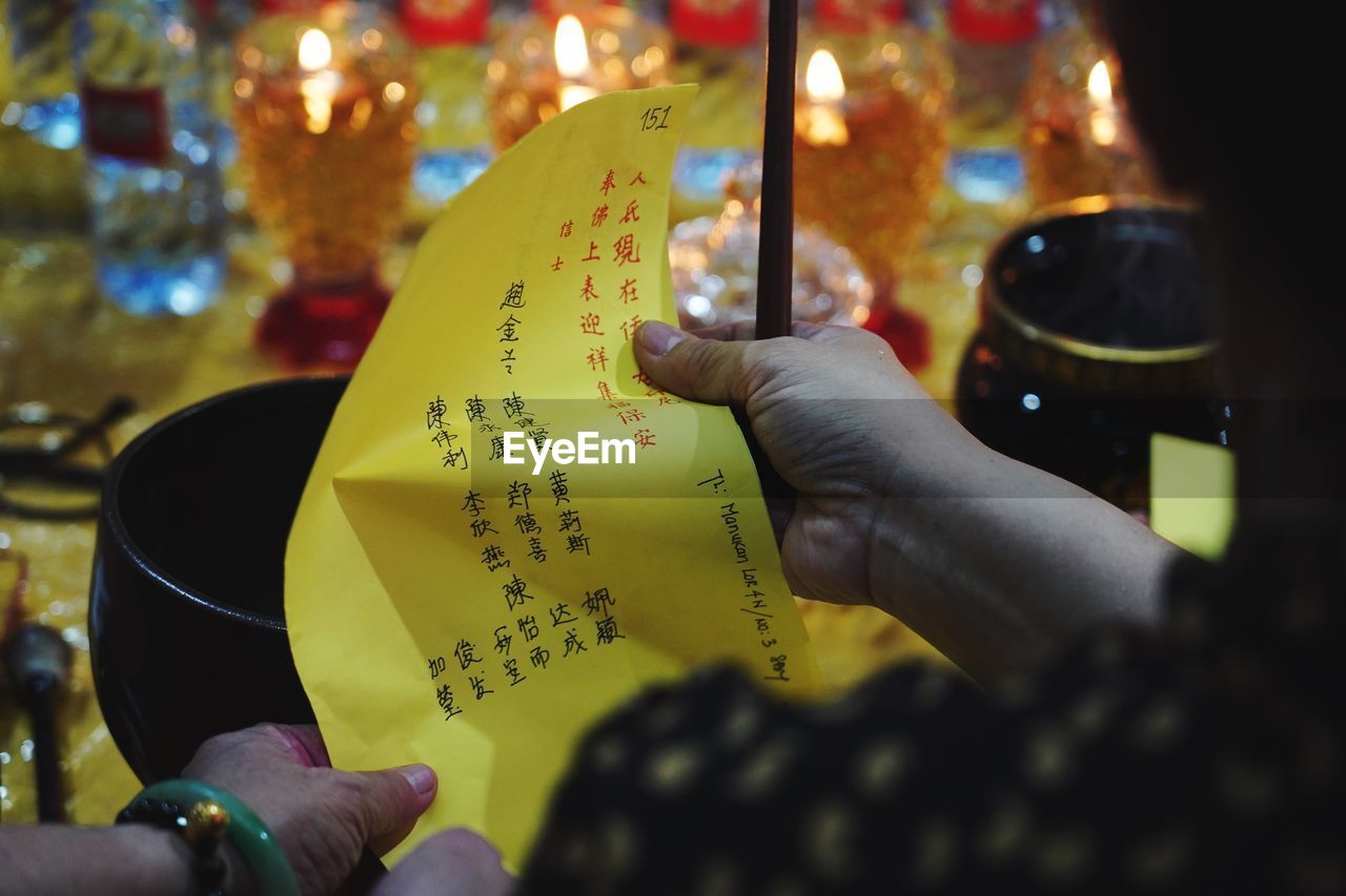 Woman, rear view, holding a yellow prayer card and some incenses. in a taoist temple