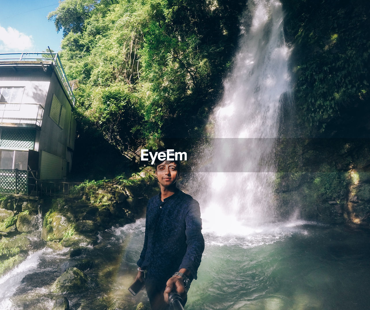 PORTRAIT OF SMILING YOUNG MAN STANDING AGAINST WATERFALL