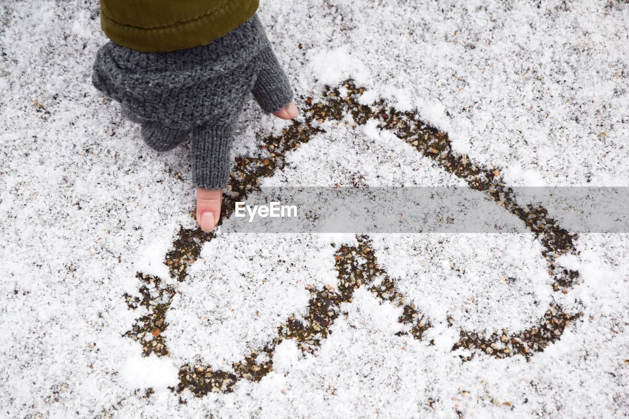 Cropped hand of woman wearing fingerless glove while making heart shape on snow during winter