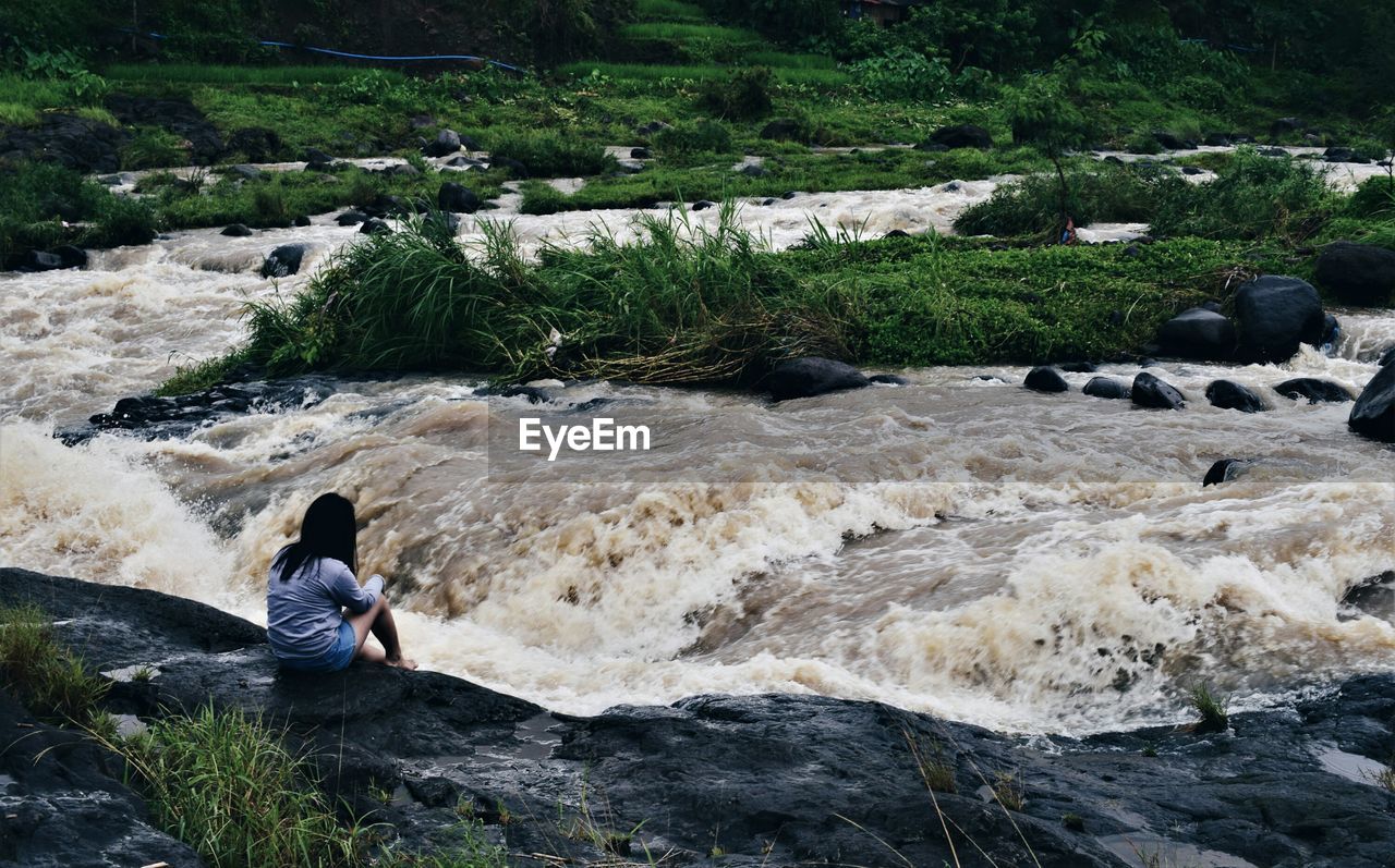 Rear view of woman sitting at riverbank