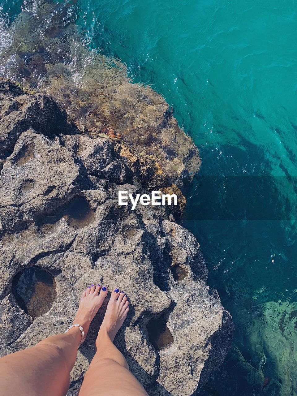 Low section of woman on rock by sea