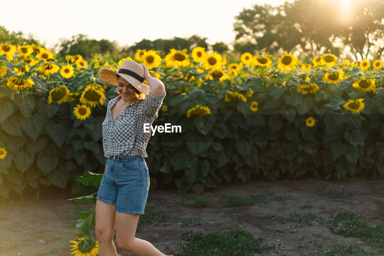 Beautiful young woman with sunflowers enjoying nature and laughing on summer sunflower field.