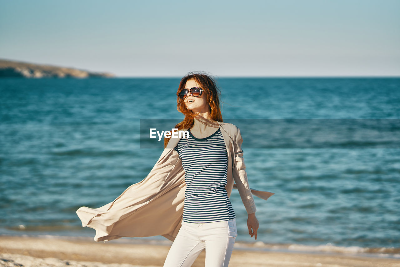 Woman wearing sunglasses standing at beach against sky