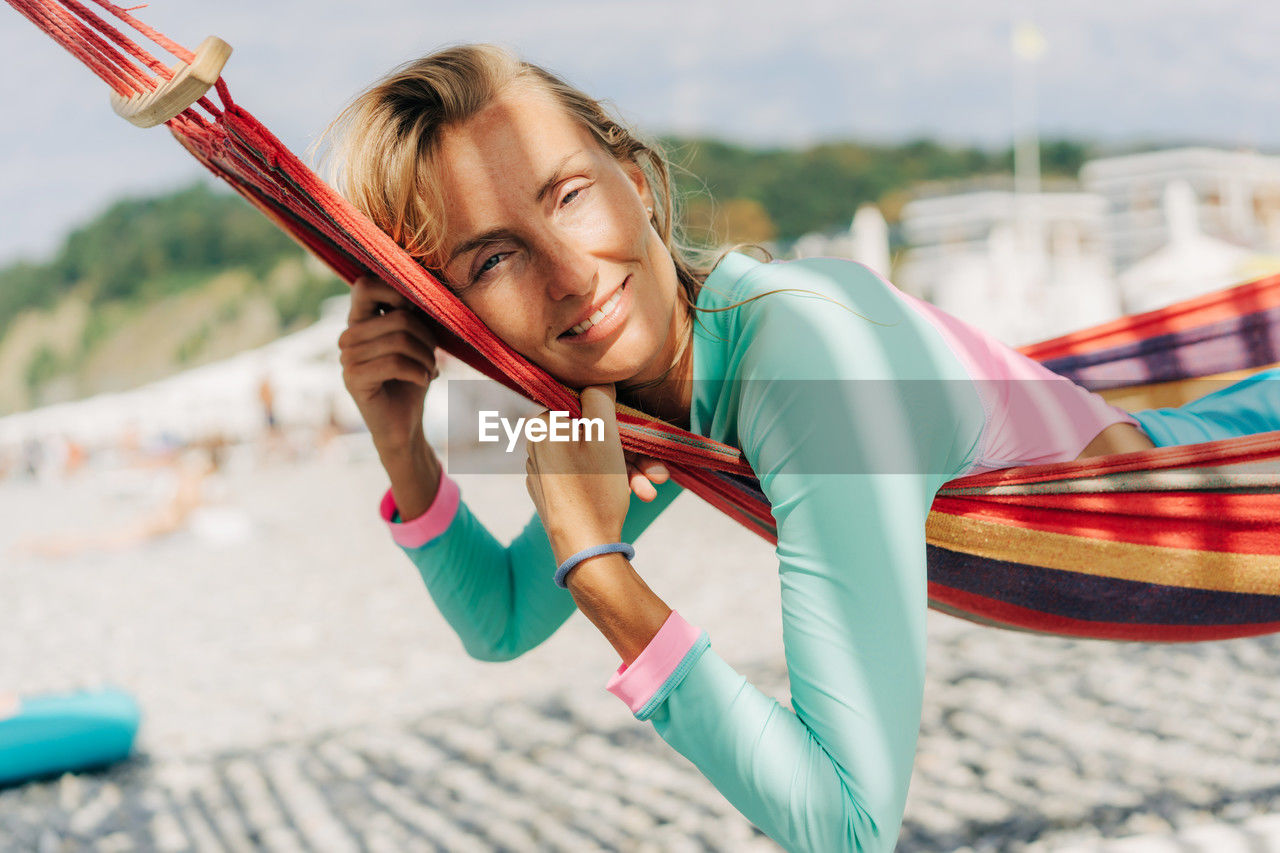 Happy smiling carefree young woman lies in a hammock on the beach.