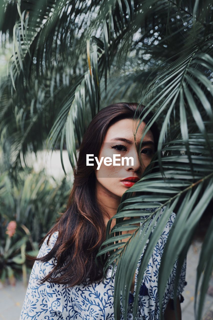 Portrait of serious young woman standing by plants in park