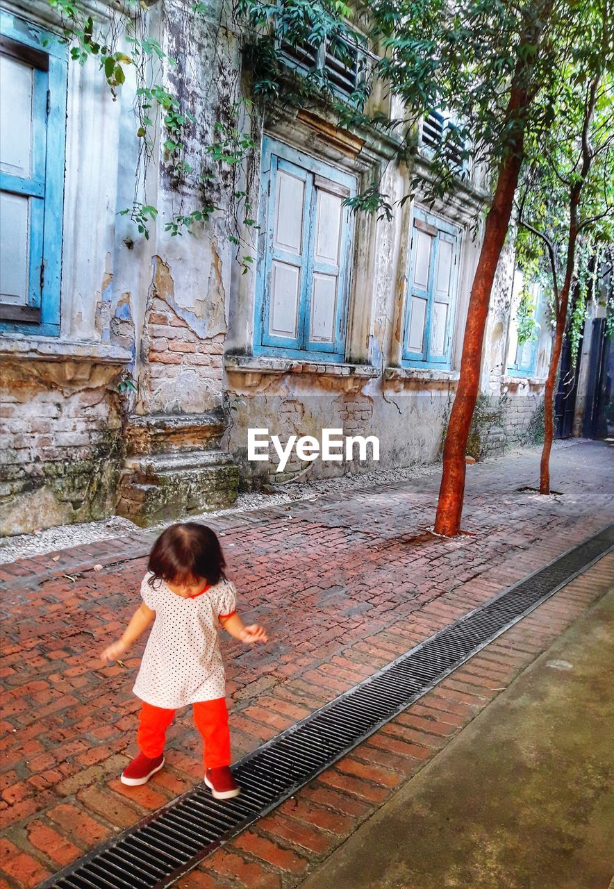 Girl standing on footpath against old building in city