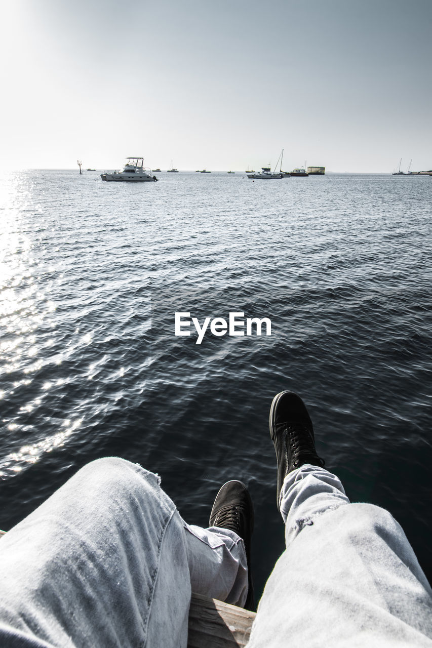 Low section of man sitting on boat sailing in sea against sky