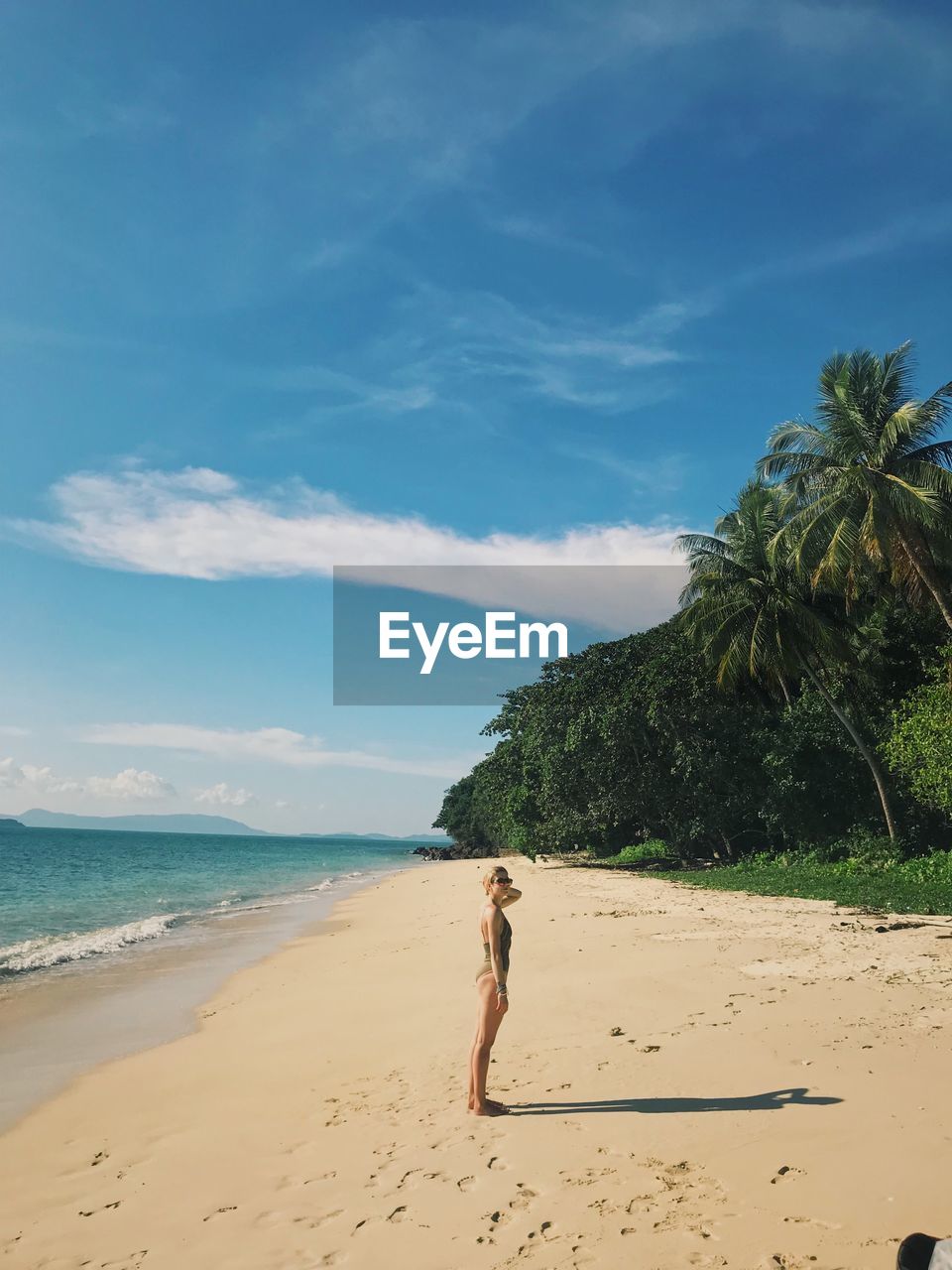 Side view of young woman standing at beach against sky