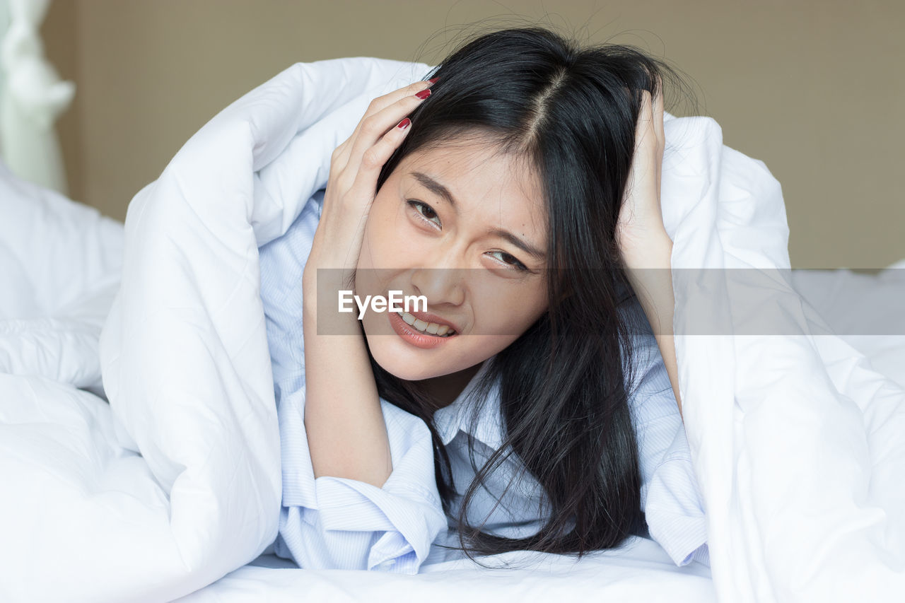 Portrait of irritated young woman touching hair lying down on bed at home