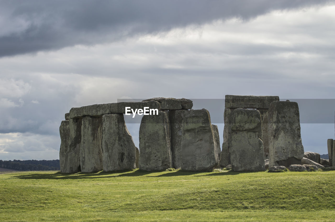 Stone structure on field against cloudy sky