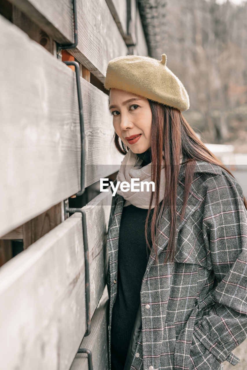 Portrait of woman wearing hat standing against wall