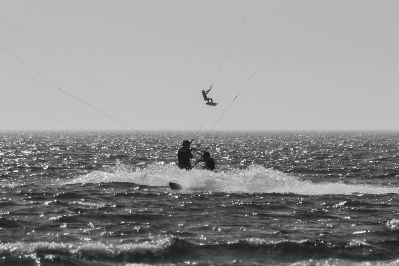 sea, water, horizon over water, sky, horizon, nature, motion, sports, black and white, extreme sports, leisure activity, kite sports, adventure, water sports, wave, one person, lifestyles, day, clear sky, beauty in nature, scenics - nature, surfing, men, monochrome photography, windsports, vacation, holiday, monochrome, trip, outdoors, sailing, wind wave, land, coast, waterfront, silhouette, enjoyment, wind, transportation, beach, sunny, sunlight