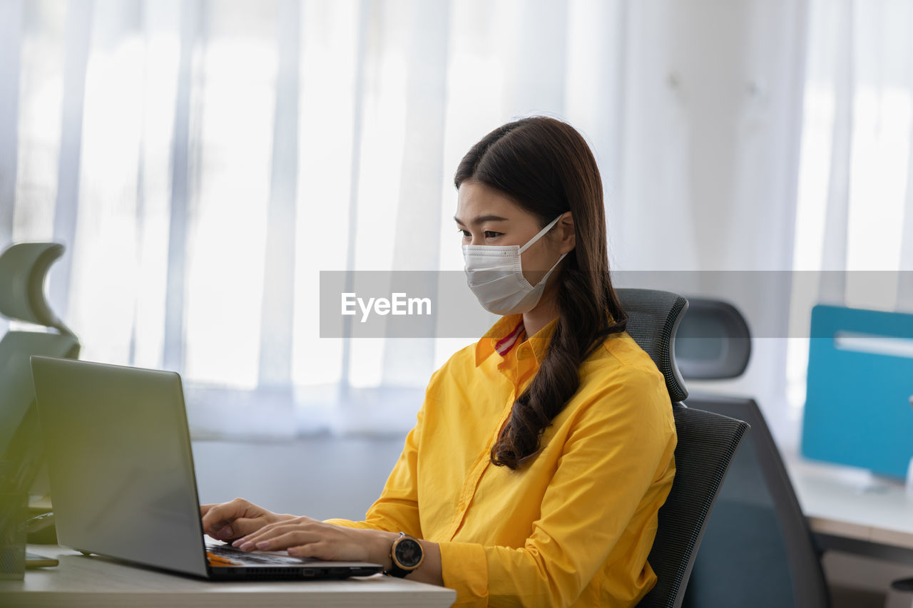 Cheerful businesswoman wearing mask using laptop in office