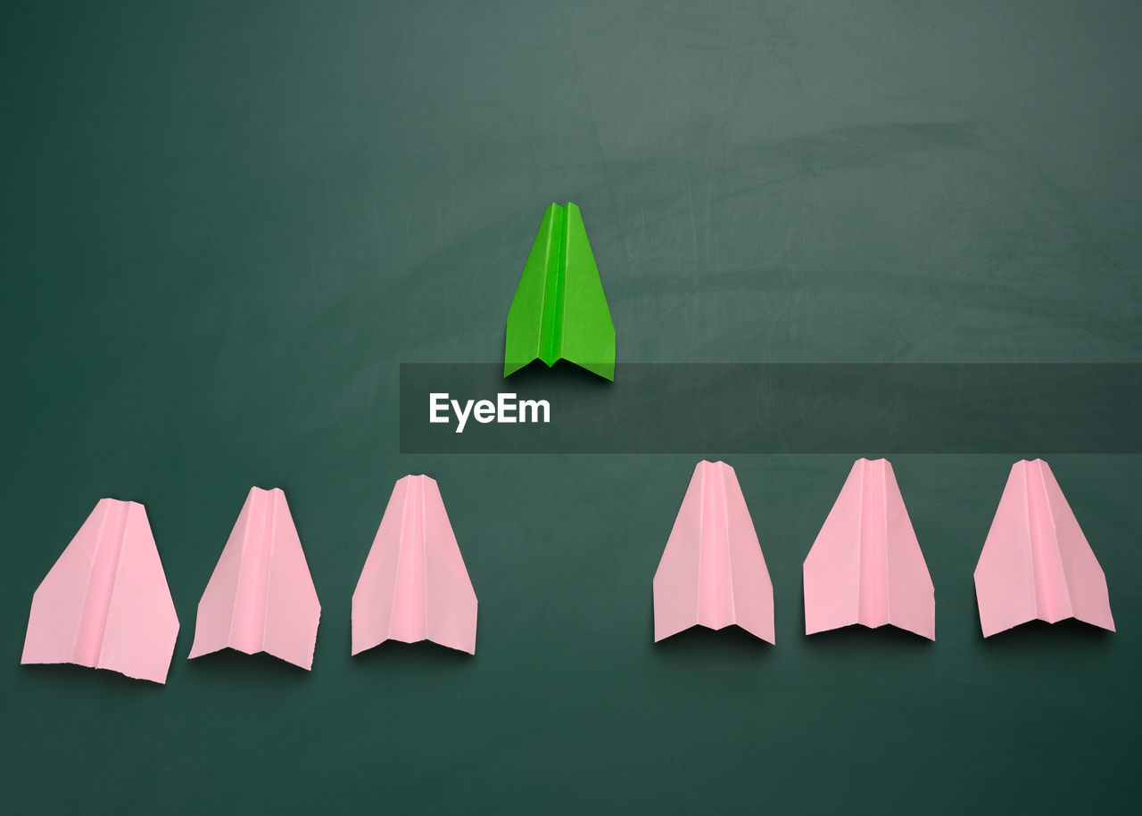 Group of pink paper planes follow the first green airplane against a green background. the concept 
