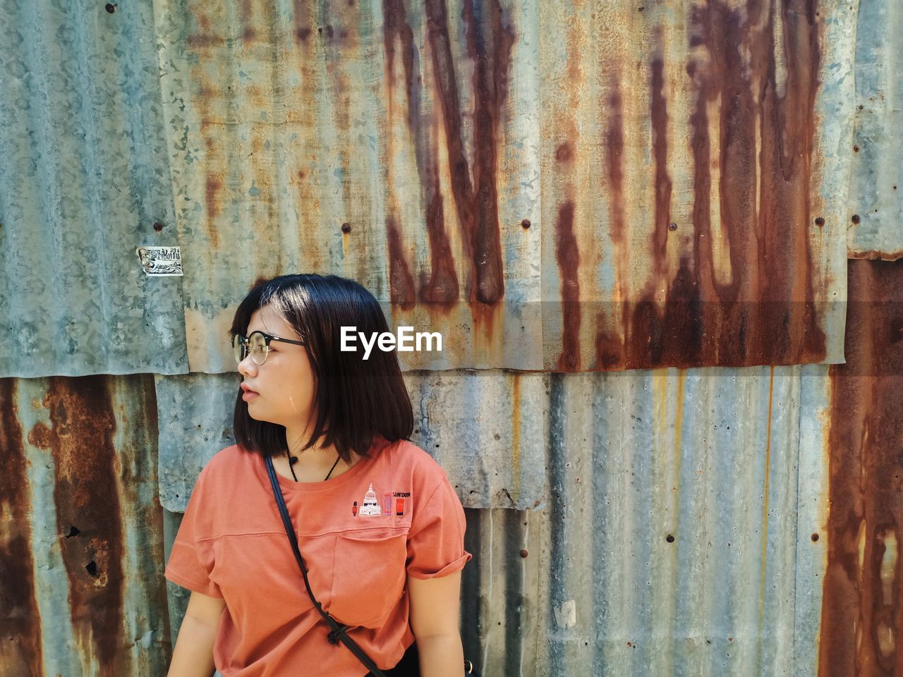 Young woman looking away while standing against corrugated iron