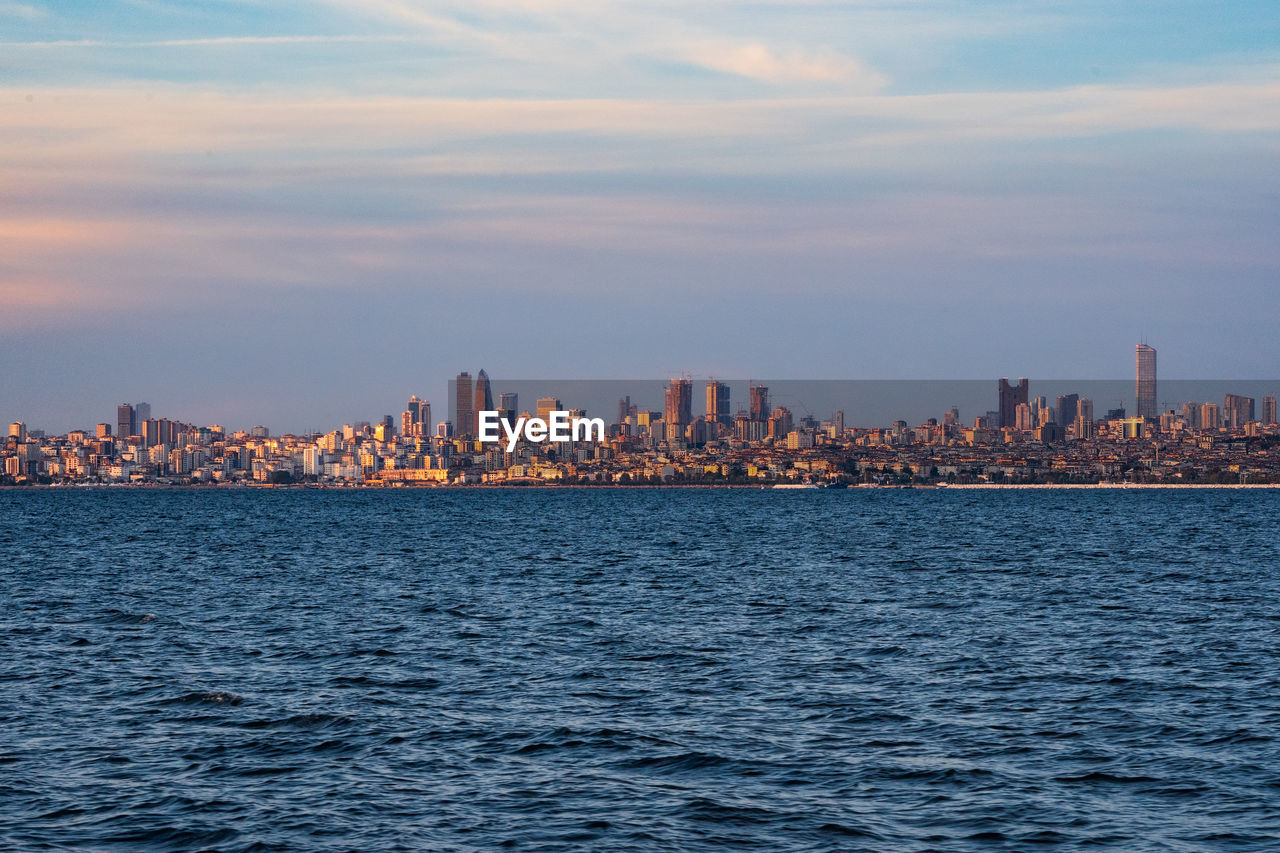 Sea by buildings in city against sky