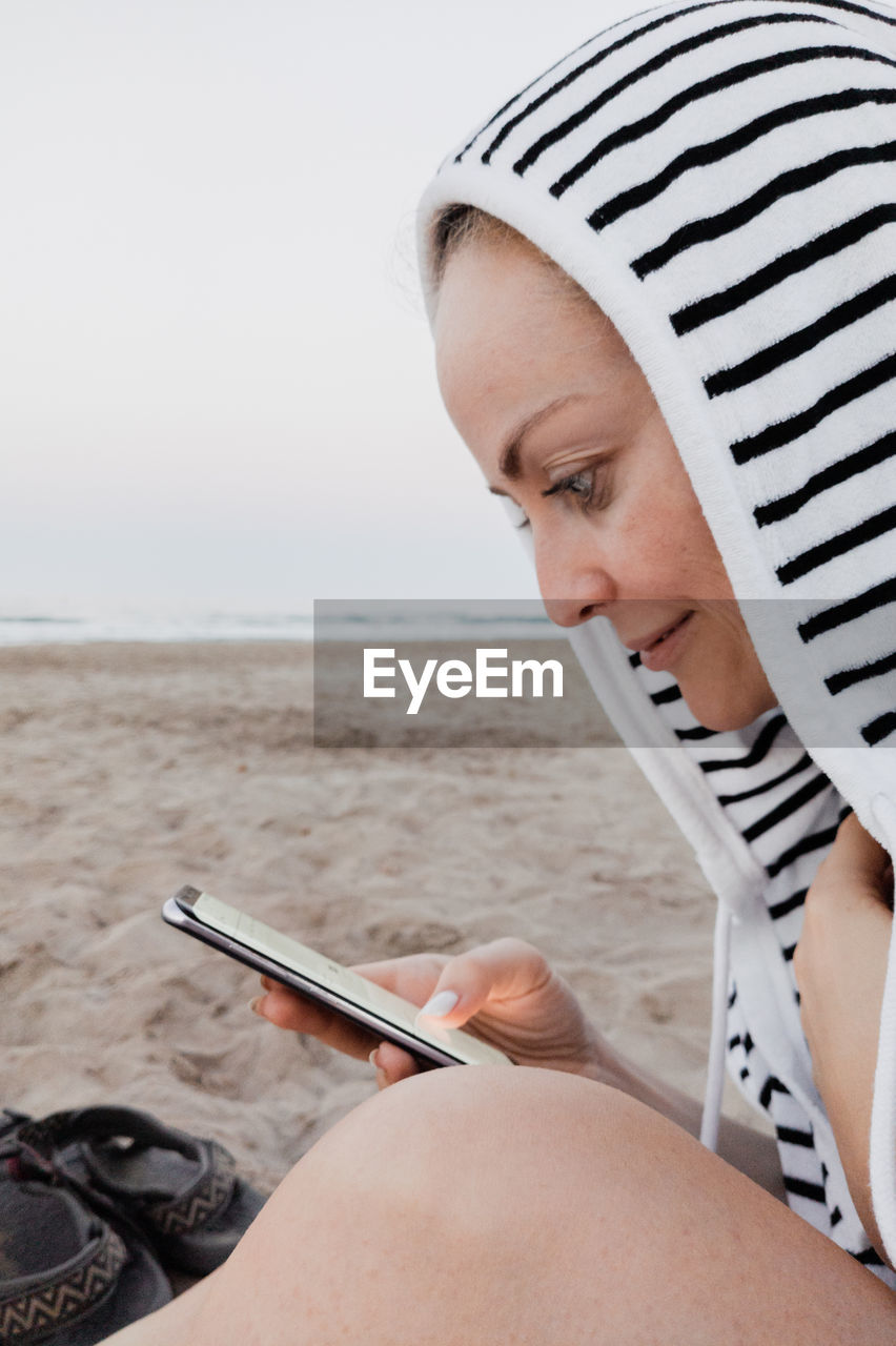 Side view of woman using smart phone sitting at beach