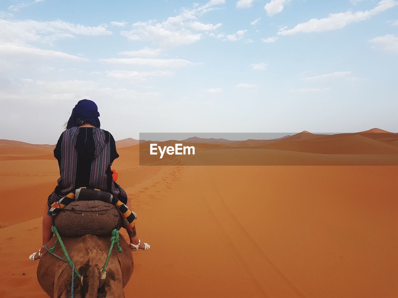 Rear view of woman riding camel at desert against sky