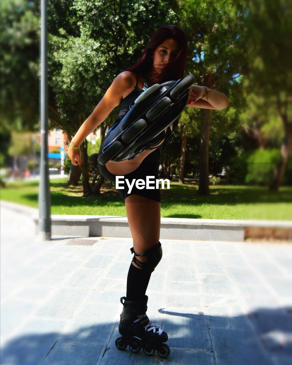 Portrait of young woman kicking while roller skating at park on sunny day