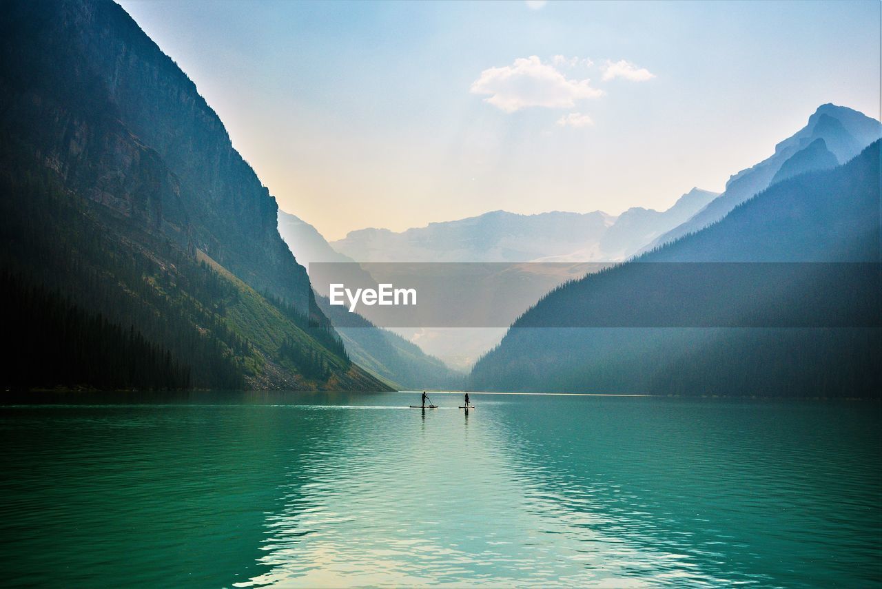 People paddleboarding in lake against mountains and sky