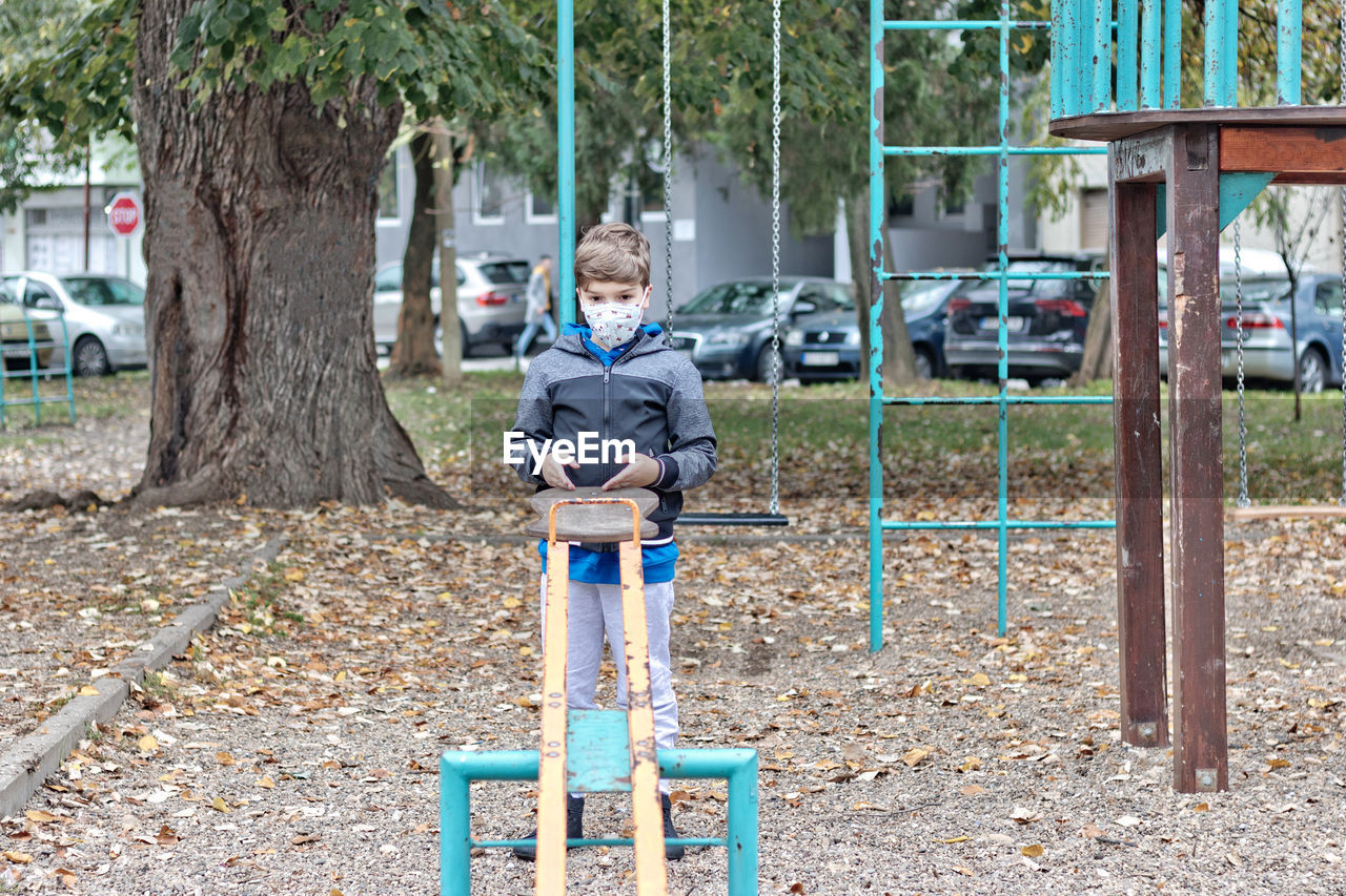 Pensive boy wearing face mask while playing alone at the playground.