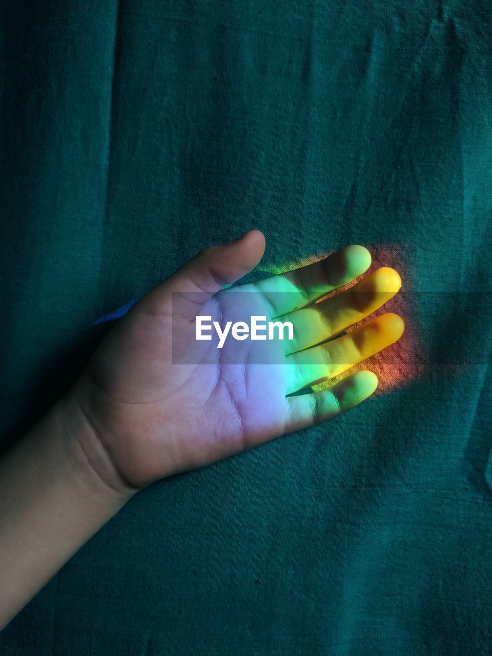 Close-up of colorful lights on cropped hand by curtain