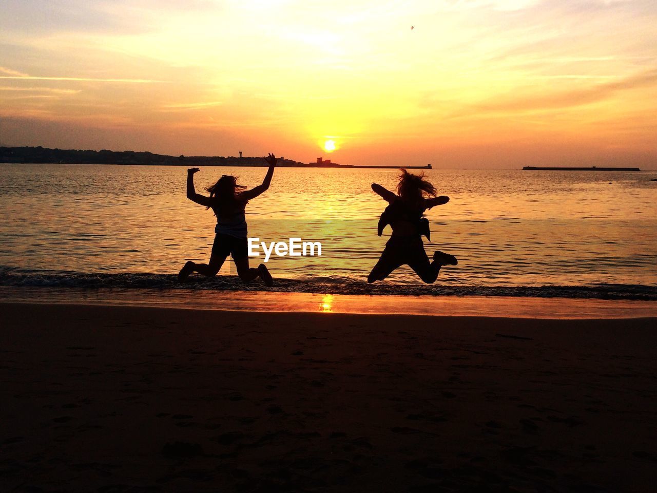 Silhouette women jumping at beach during sunset