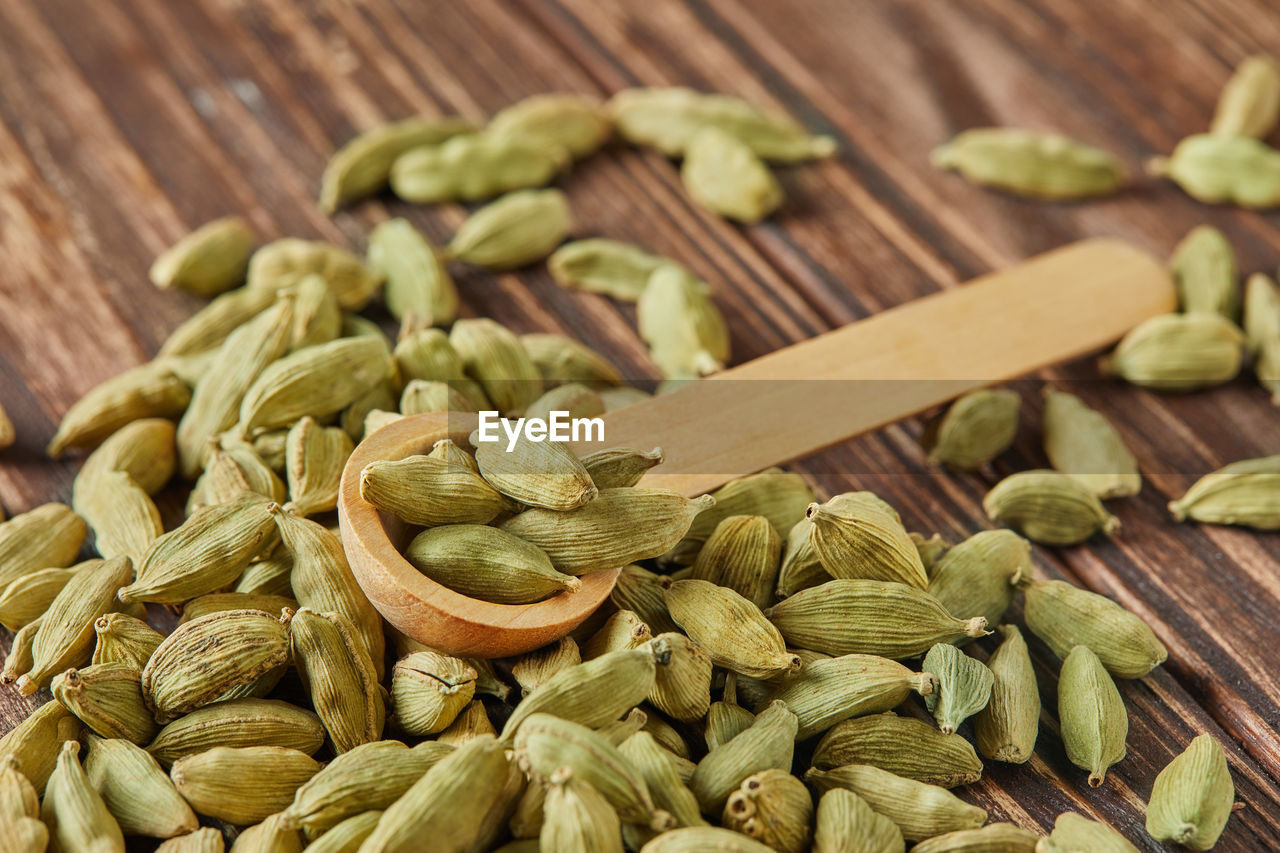 Green cardamom with wooden spoon scattered over vintage wooden background