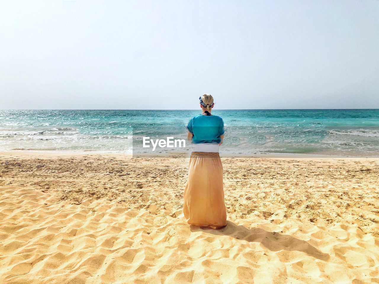 REAR VIEW OF WOMAN STANDING AT BEACH AGAINST SKY