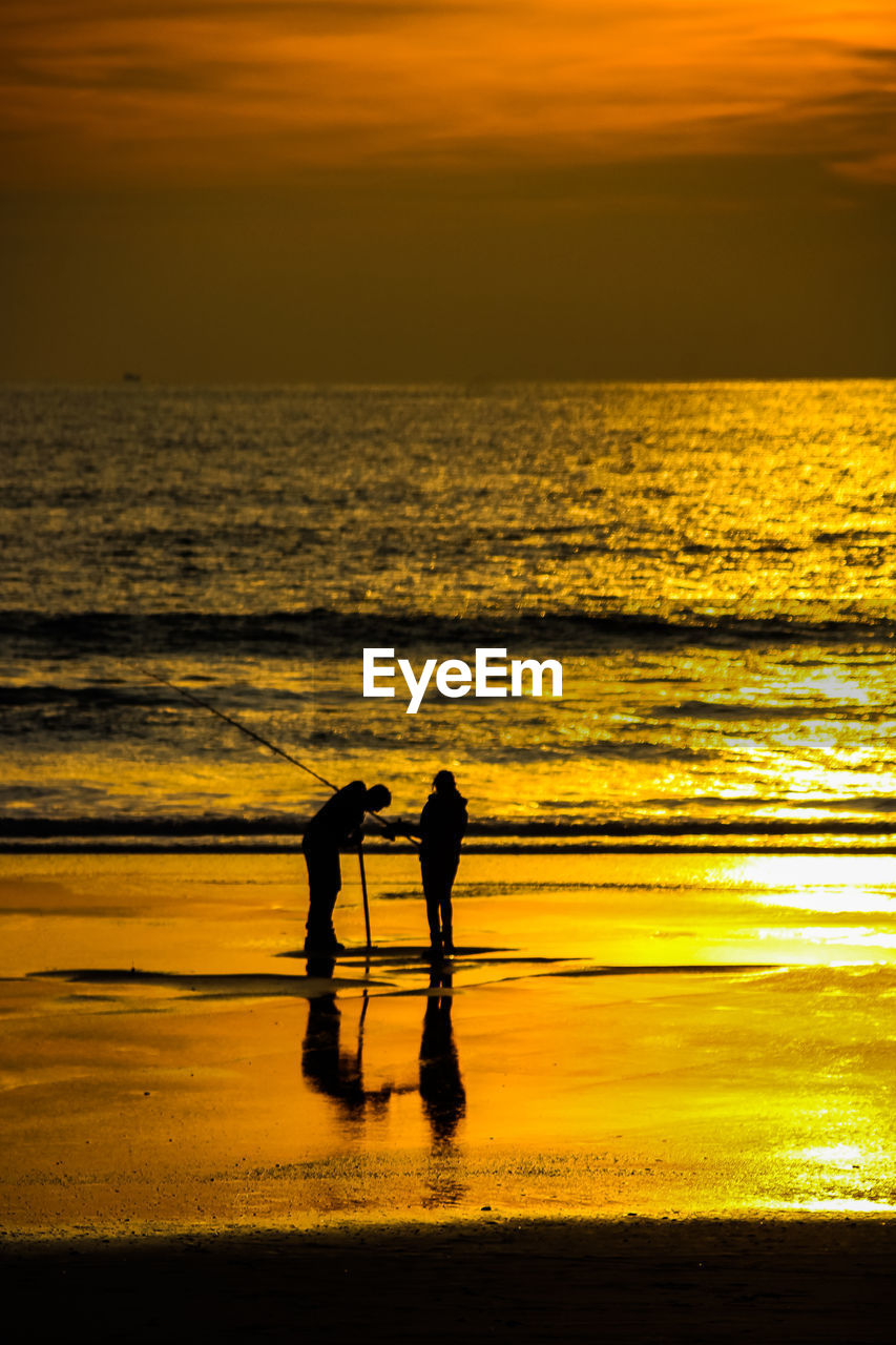 Silhouette people on beach against sky during sunset