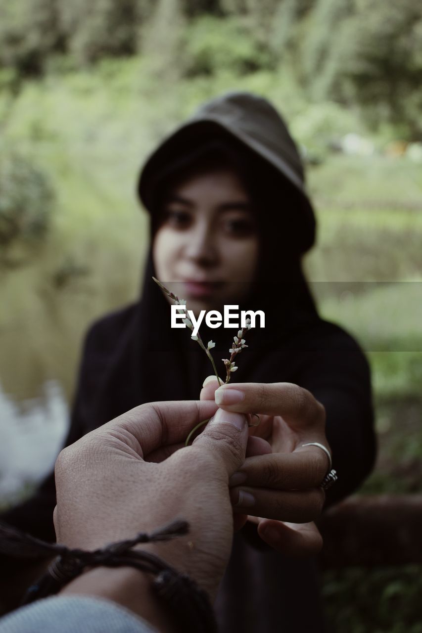 Cropped hand giving flower to woman