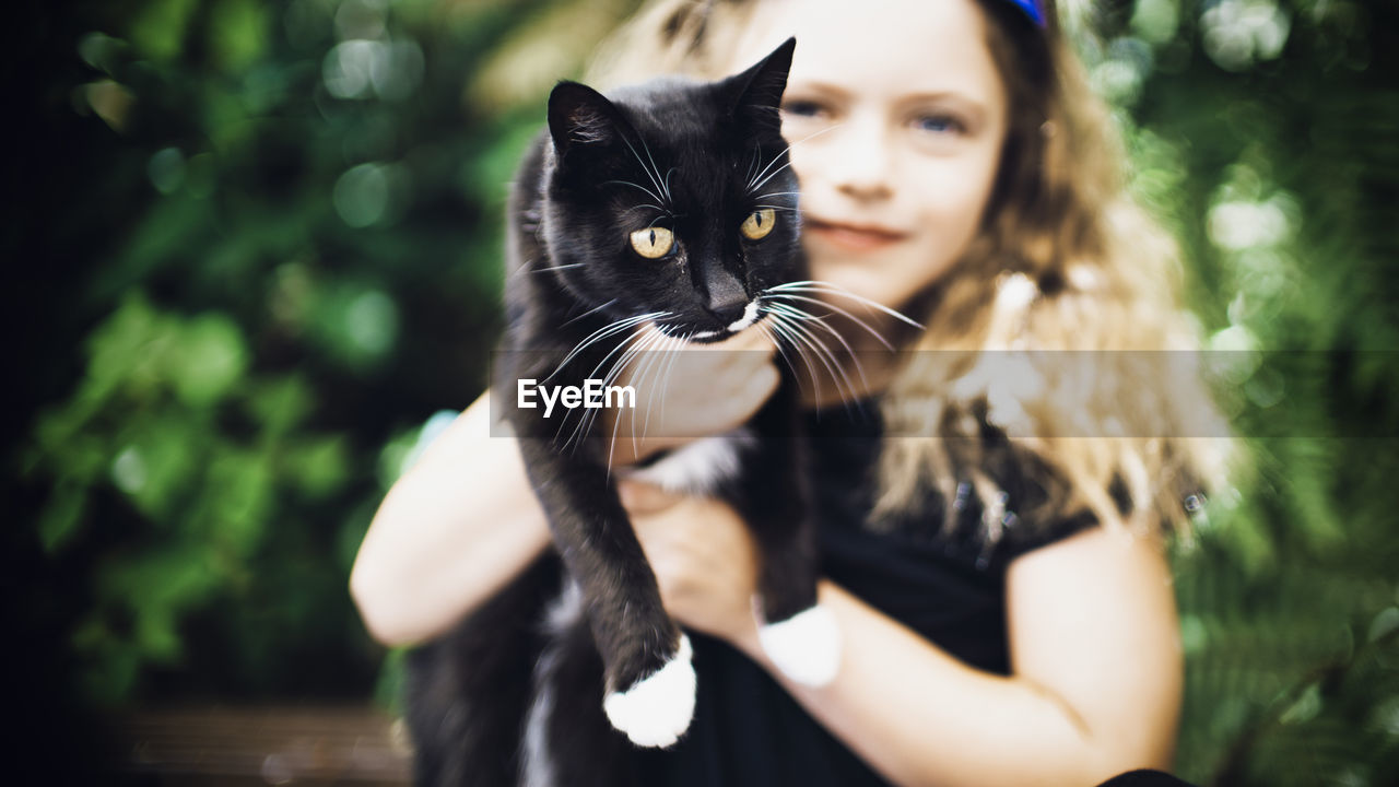 Portrait of cute girl holding black cat while standing outdoors
