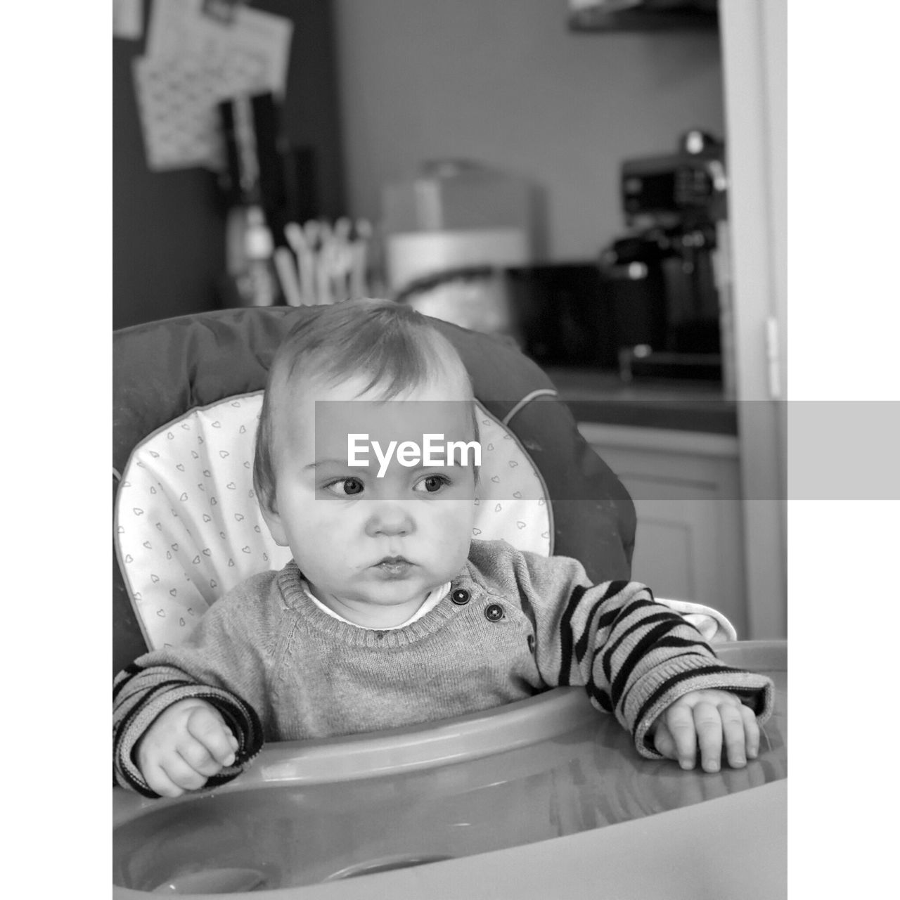 Cute baby boy looking away while sitting on high chair at home